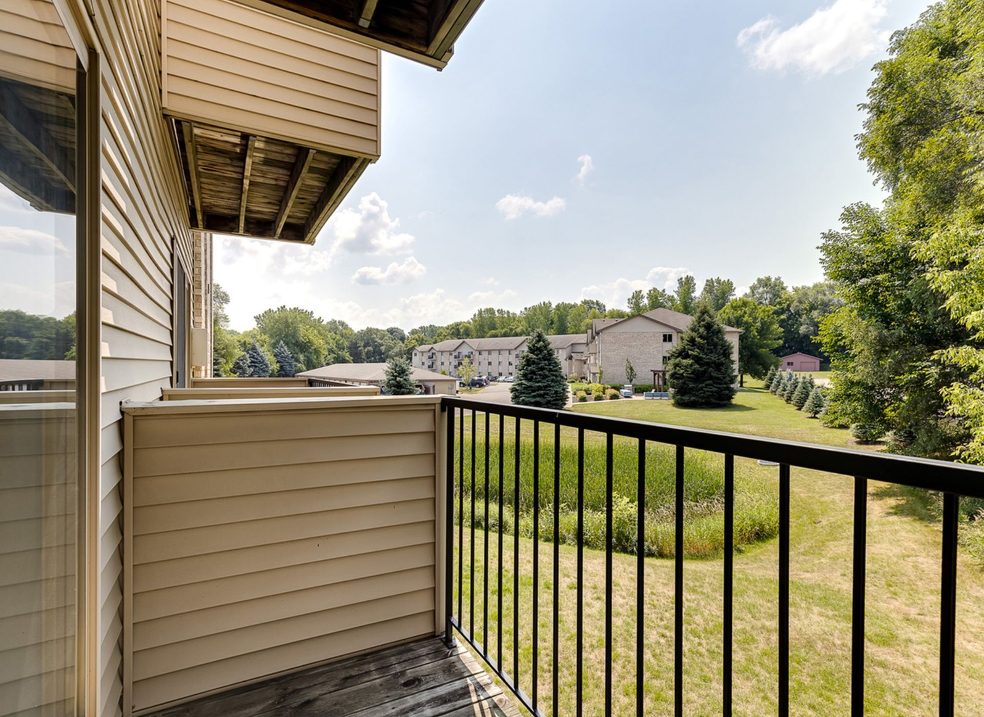 Balcony view from an apartment overlooking the community grounds with buildings and trees.