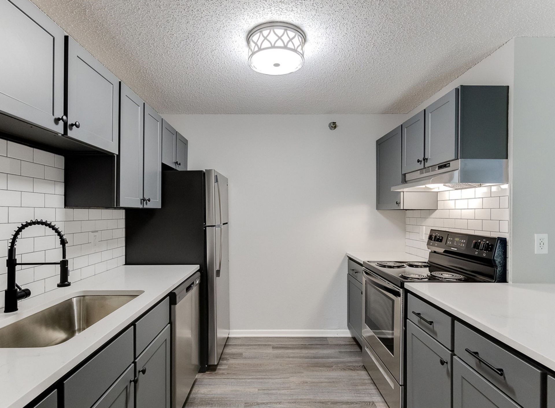 Modern gray kitchen with stainless steel fridge, stove, dishwasher, white counters, and subway tile backsplash.