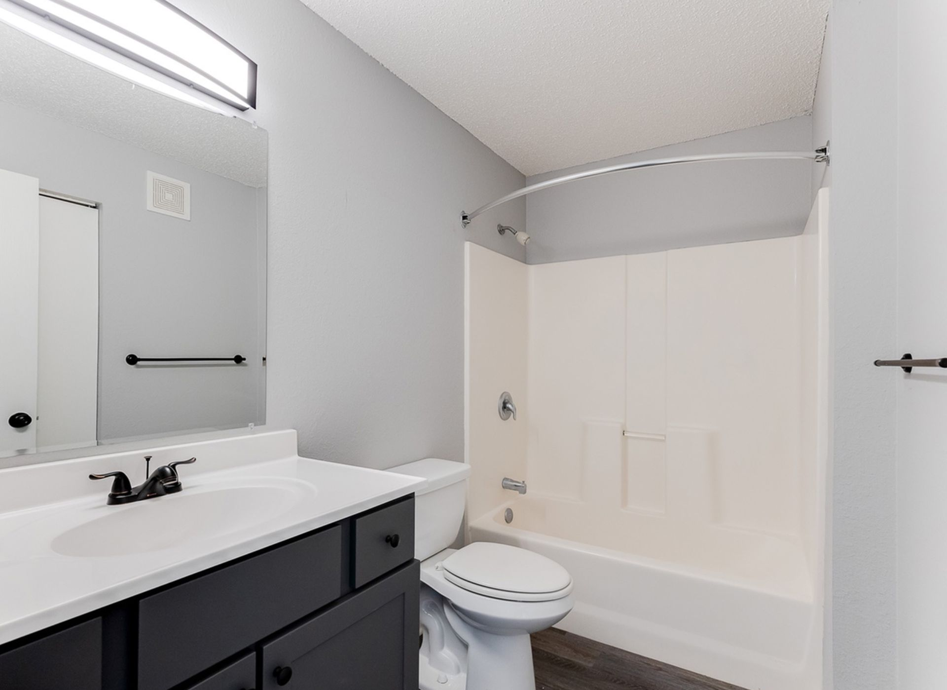 Bathroom with white vanity, dark cabinetry, toilet, and tub/shower combo.