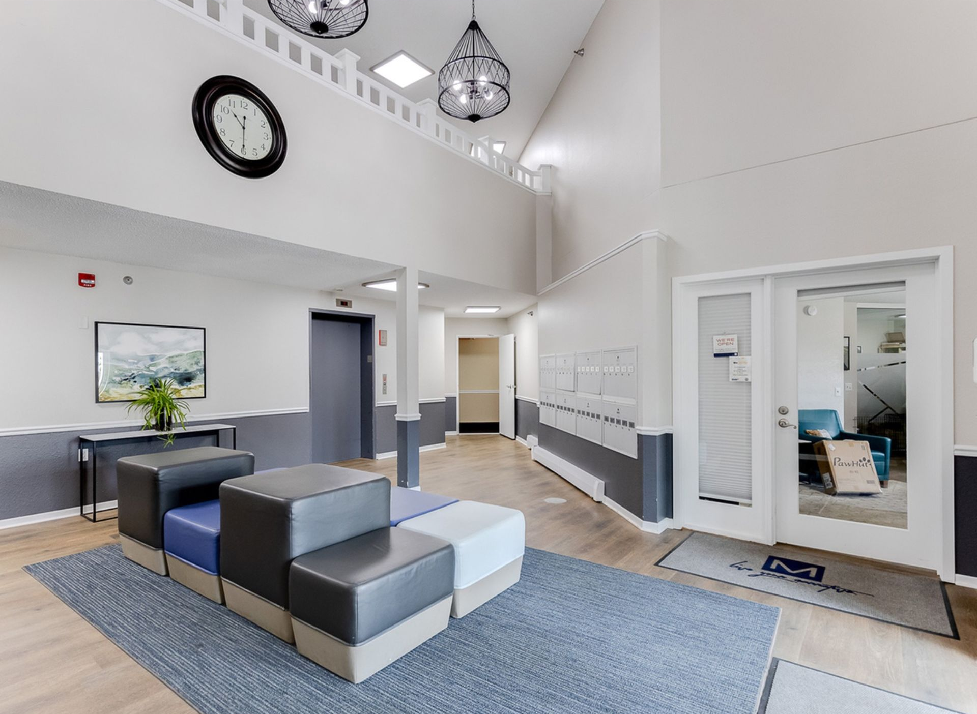 Interior community lobby with modern seating, a wall of mailboxes, and a large clock.