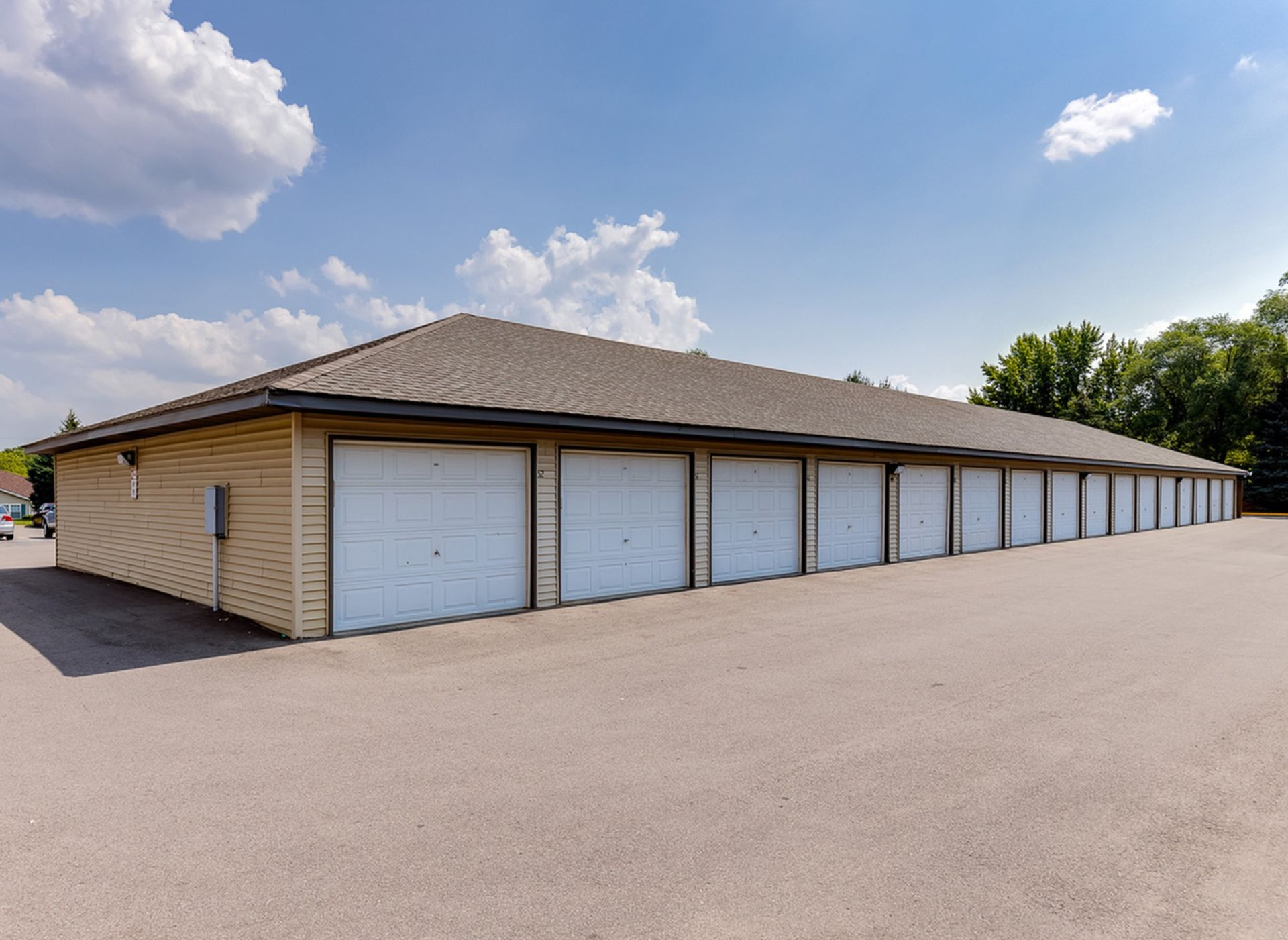 Long row of beige storage units with white doors along a paved lot under a clear blue sky.