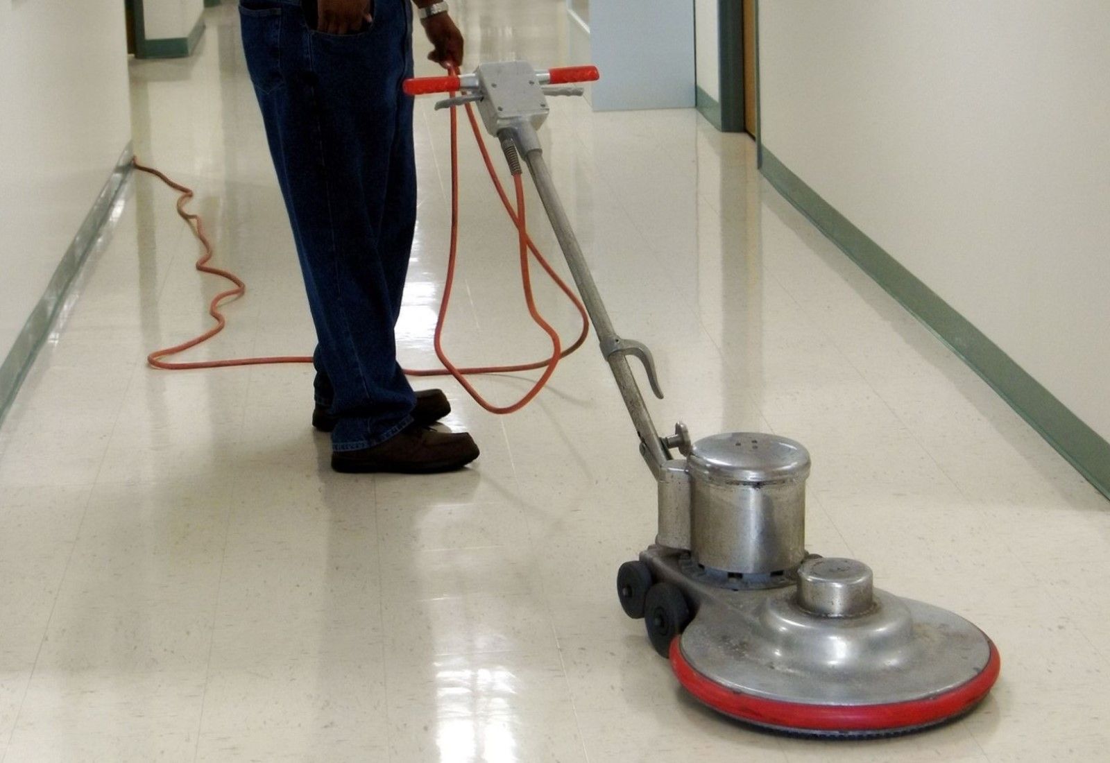 Person operating a floor buffer in a hallway, with red cords trailing on the floor.