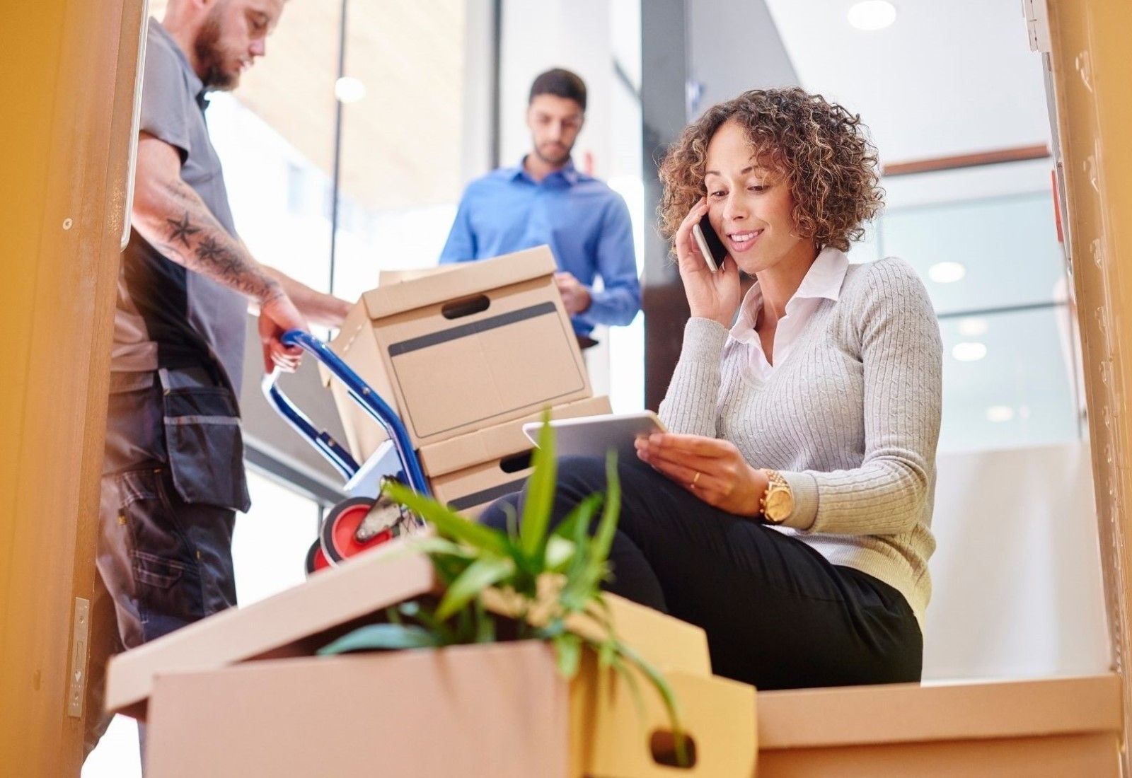 People packing boxes in a bright office with a cart and plants during a move