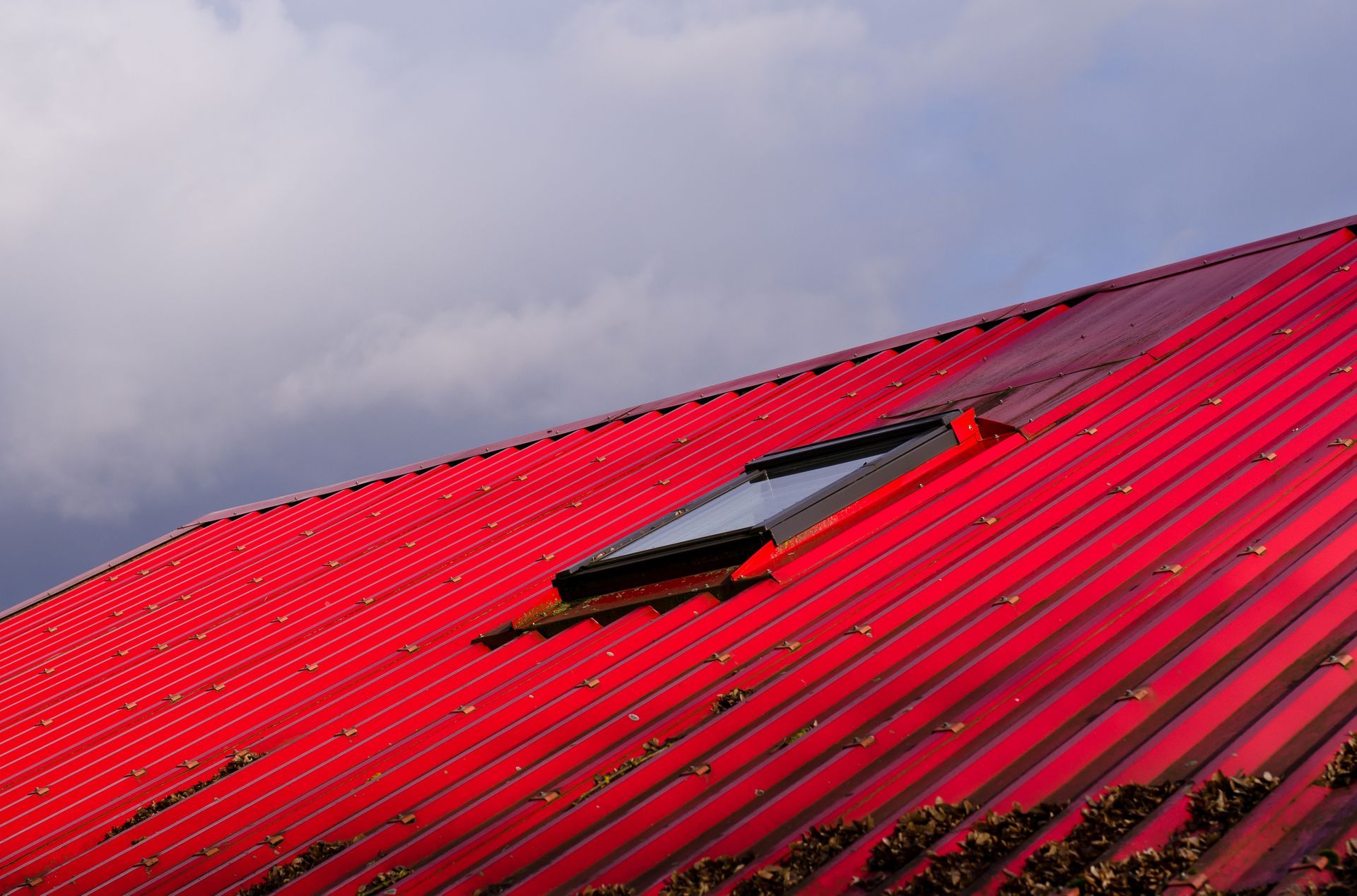 Red corrugated metal roof with a skylight against a cloudy sky