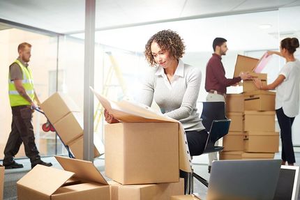 People moving boxes in a bright office during a relocation.