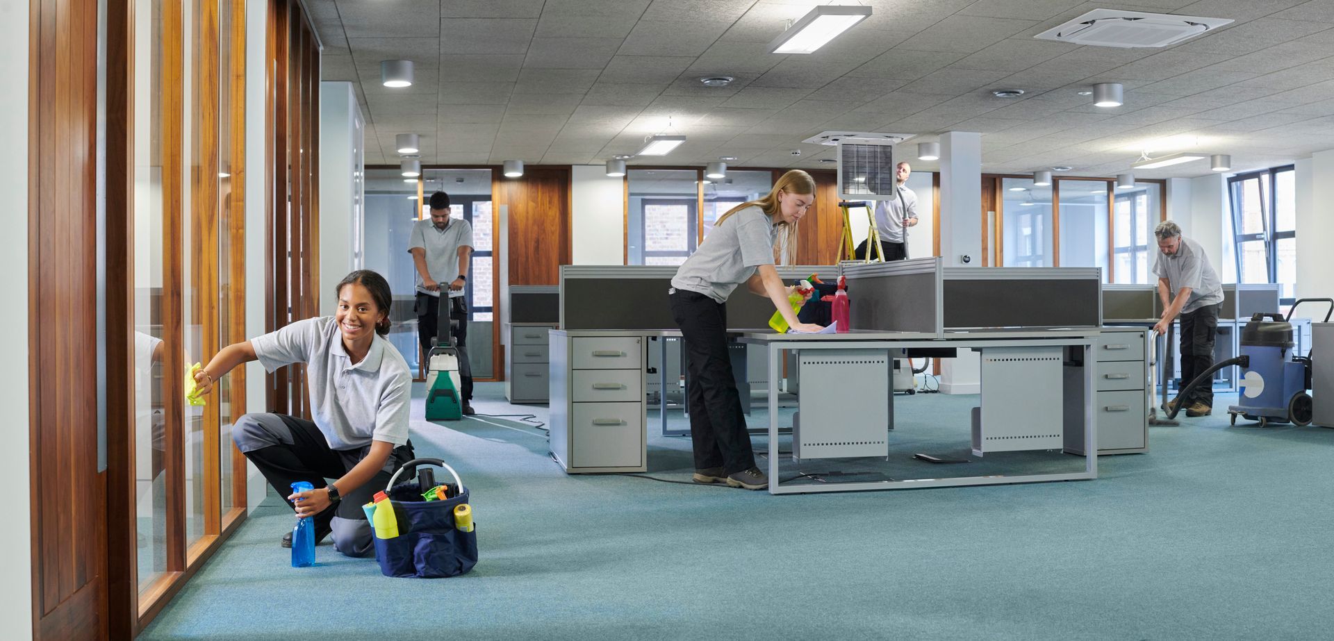 Office lobby with people working, a seated person beside a blue bag, and desks in the background