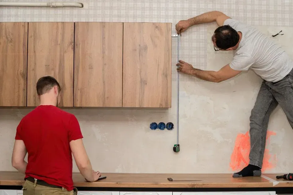 Two workers installing wall panels and leveling a hanging board in a workshop.