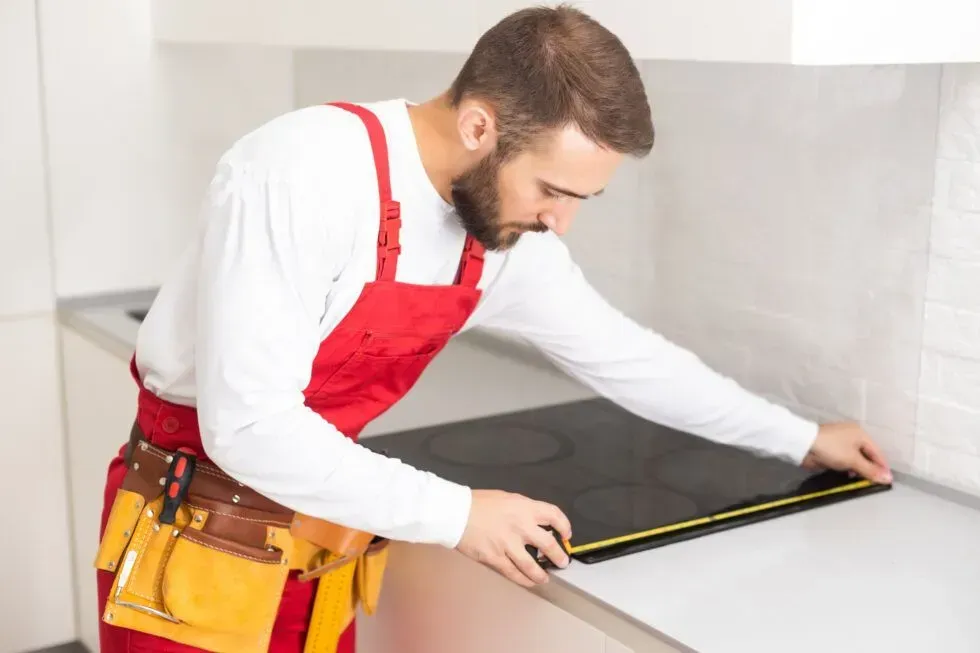 Worker in red apron measuring a countertop with a tape measure in a kitchen.
