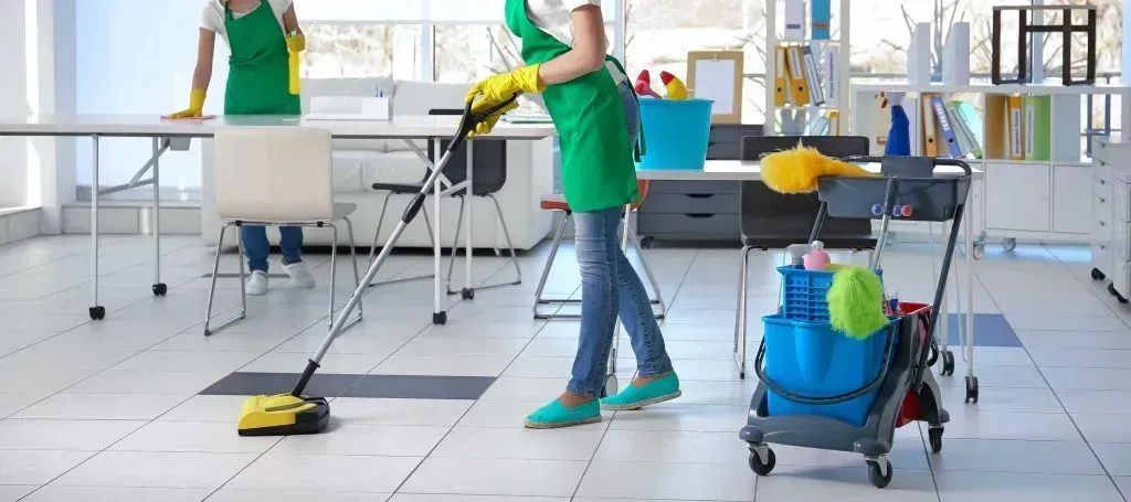 Two cleaning staff in green uniforms mopping a bright tiled floor in a lab