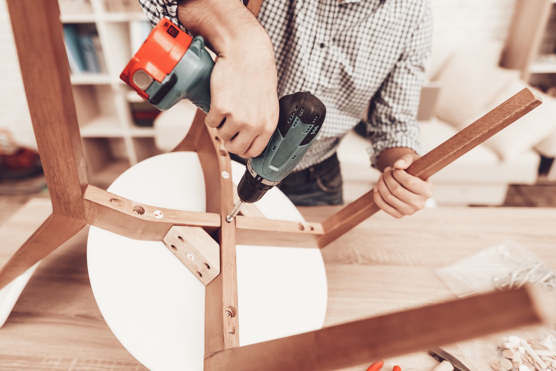 Person assembling a wooden chair with a power drill in a workshop