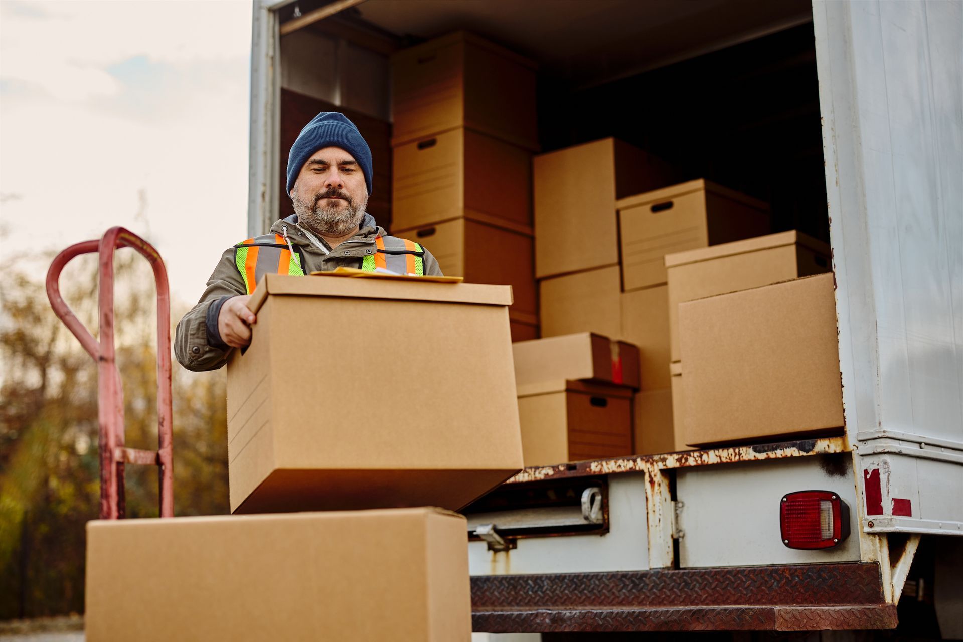 Worker carrying a cardboard box from a moving truck filled with packed boxes