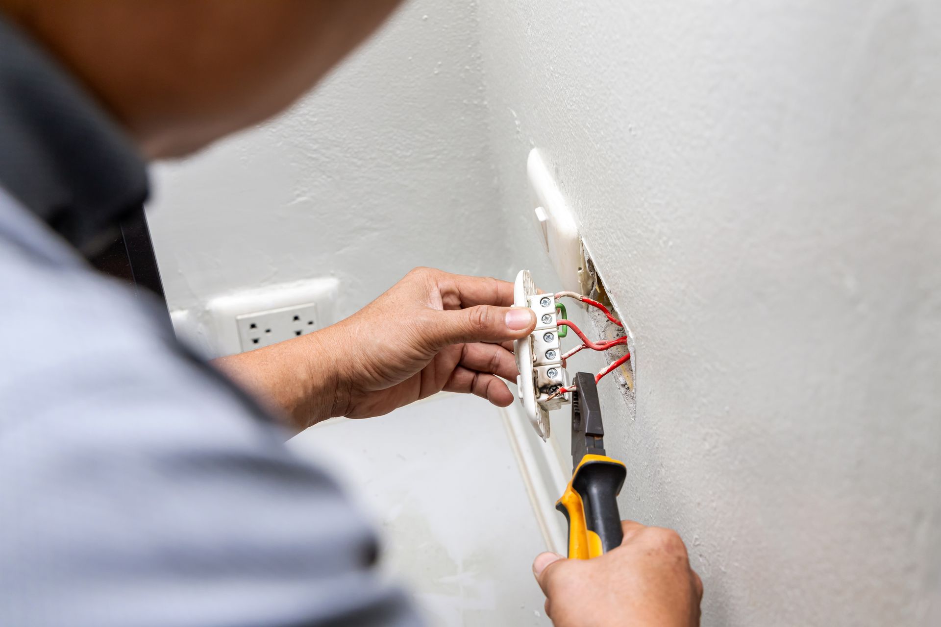 Person wiring an electrical outlet on a wall with pliers and tools