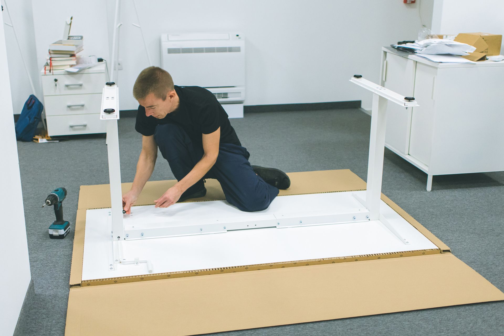 Person assembling a white table frame on a cardboard sheet in a workshop-like room