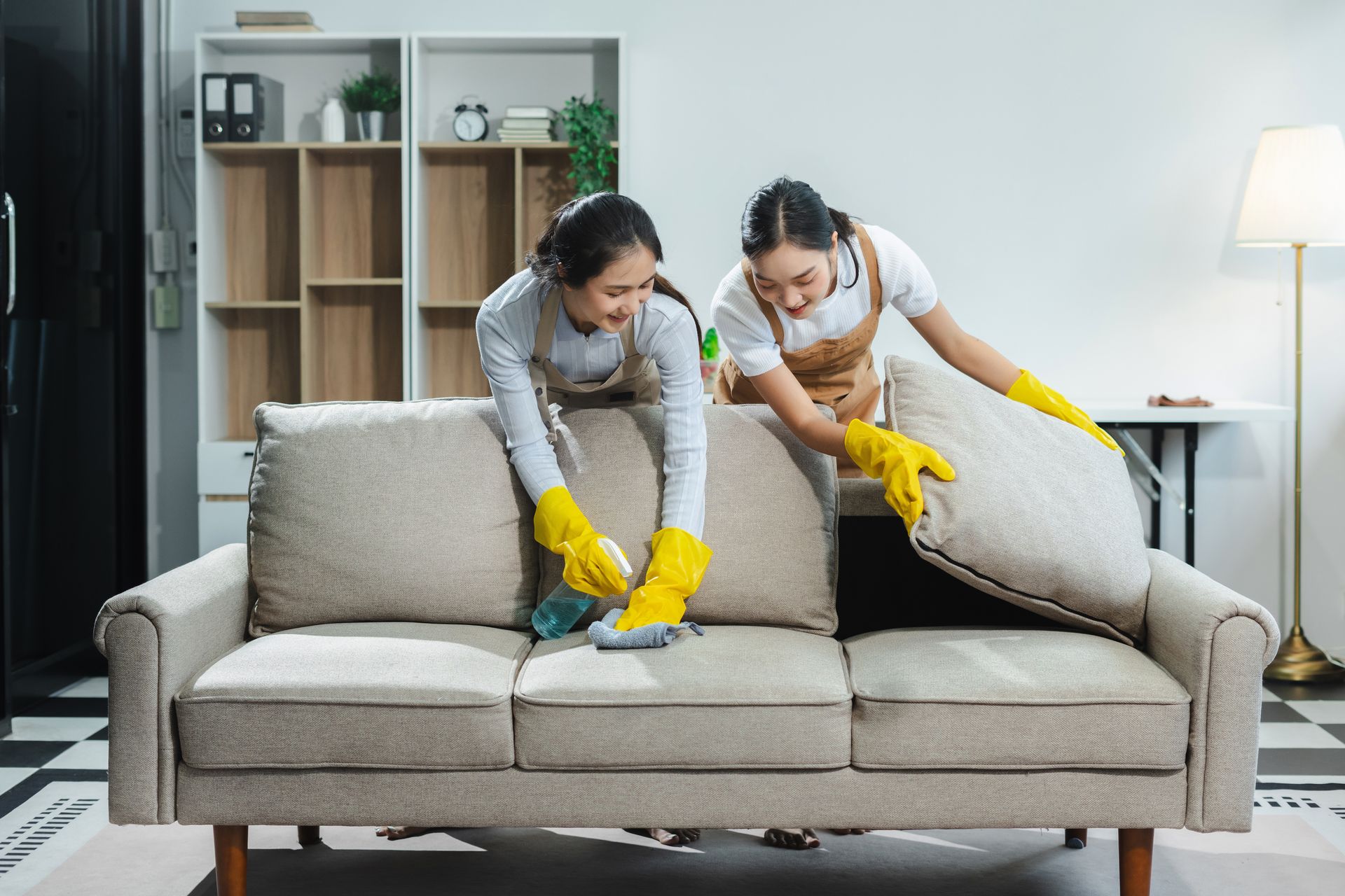 Two women are cleaning a couch in a living room. company cleaning house
