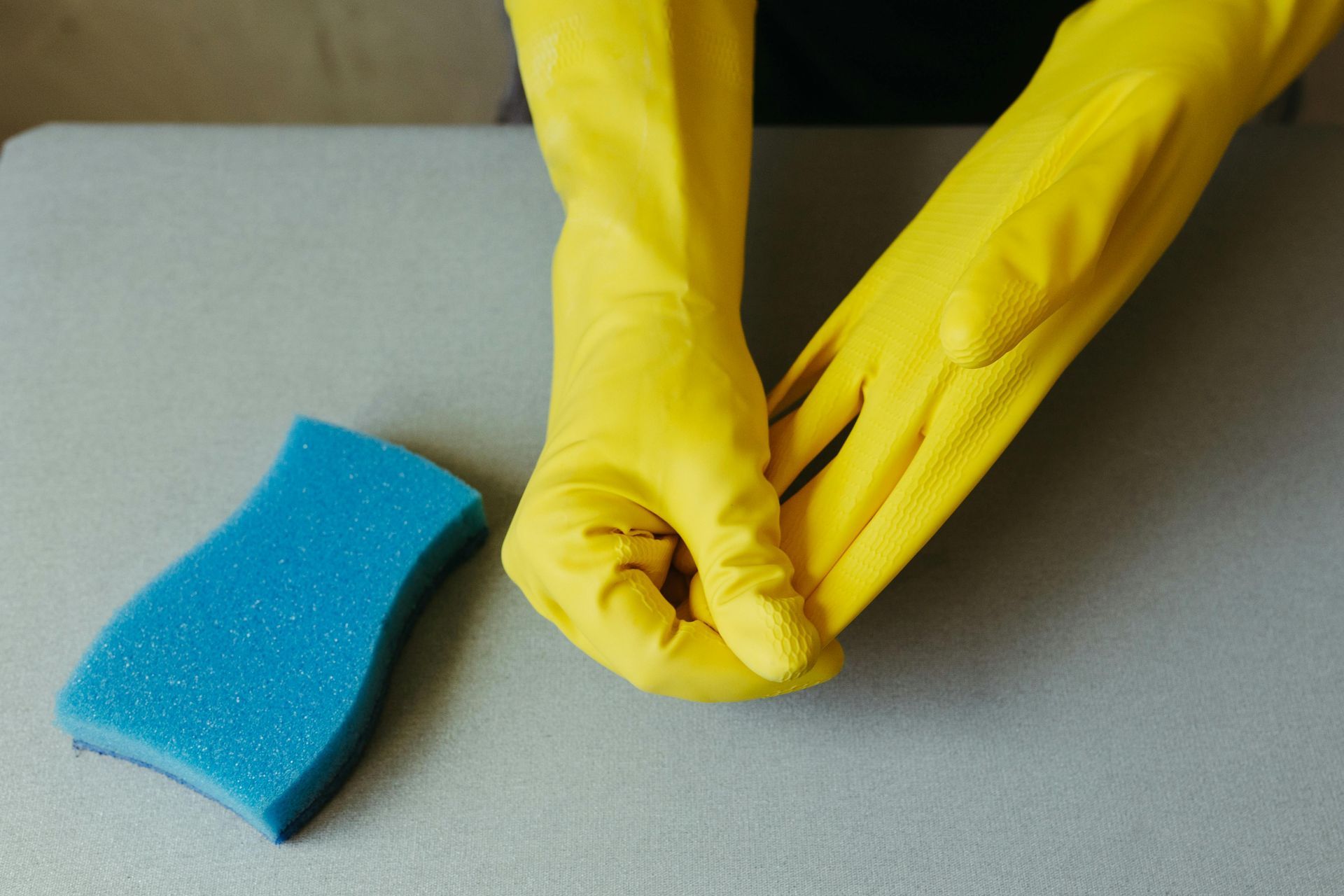 regular home cleaning A person wearing yellow rubber gloves is holding a blue sponge.
