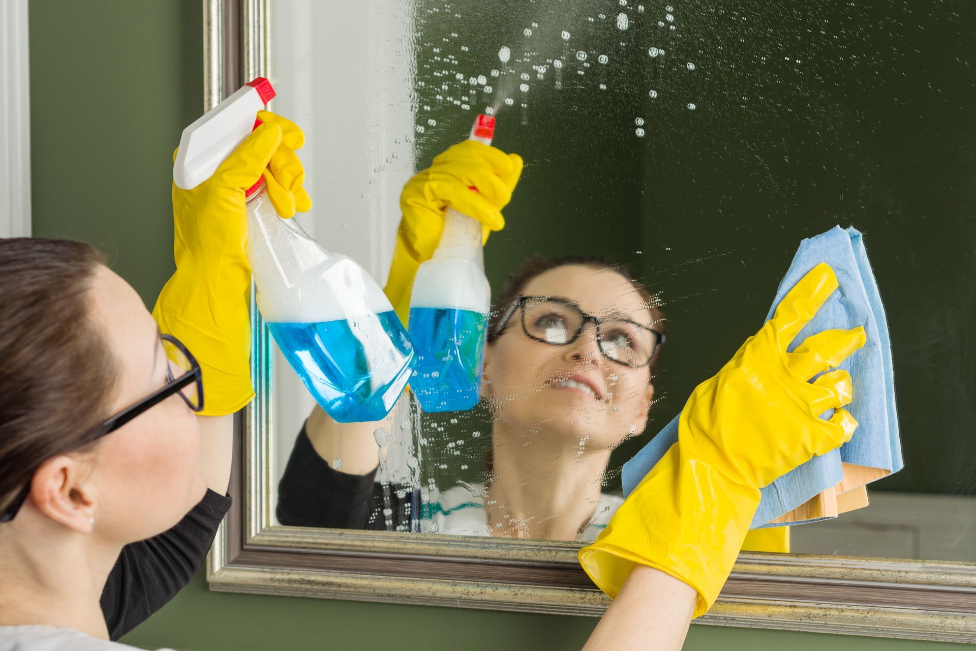 airbnb cleaning service A woman is cleaning a mirror with a spray bottle and a cloth.