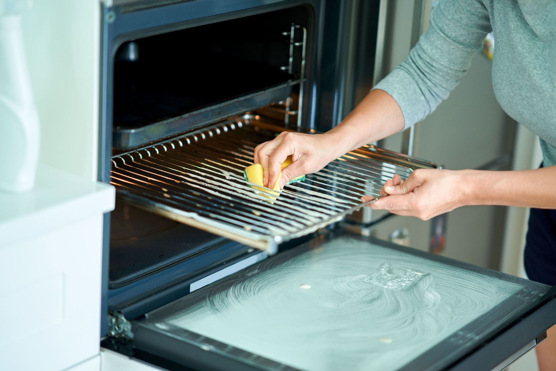 A woman is cleaning the inside of an oven with a sponge. home cleaning and services