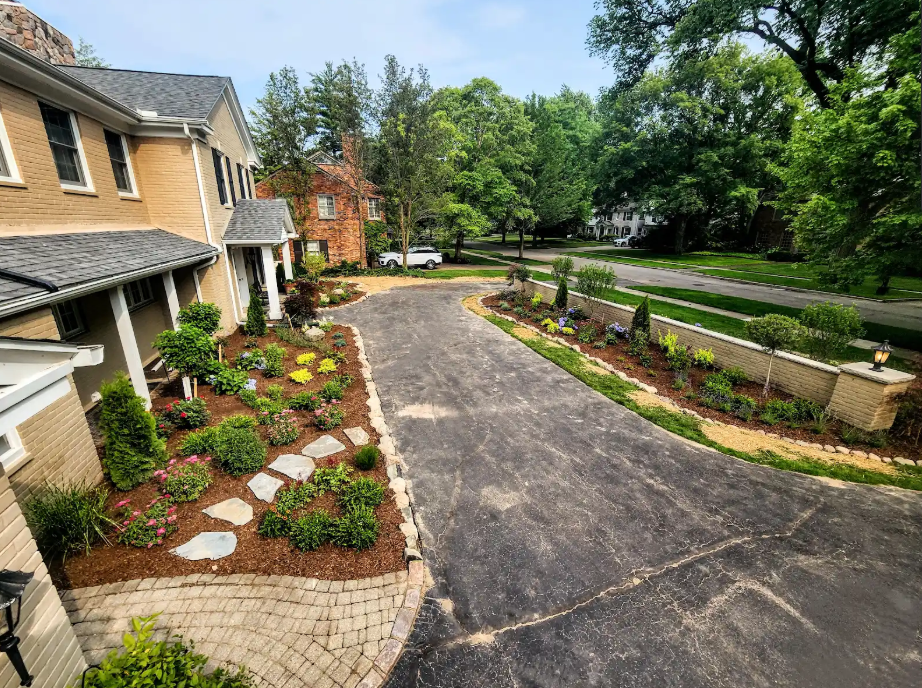 Residential driveway and landscaped garden beside a house, with stone path and trees lining the road.