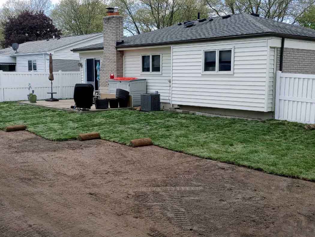 Backyard with a small white house, gravel area, grass, patio furniture, and a fence