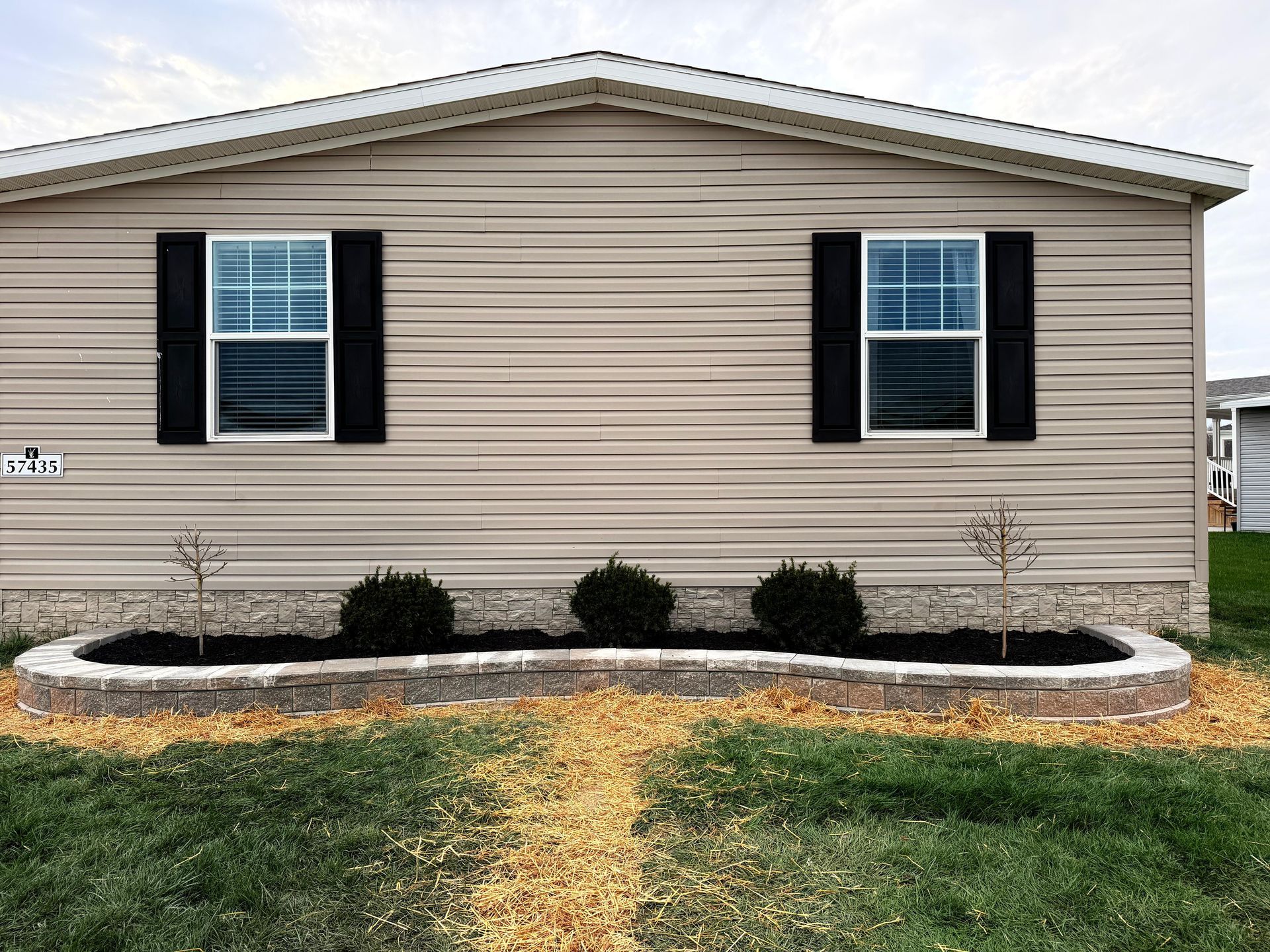 Single-story beige house with black shutters and a small landscaped front bed