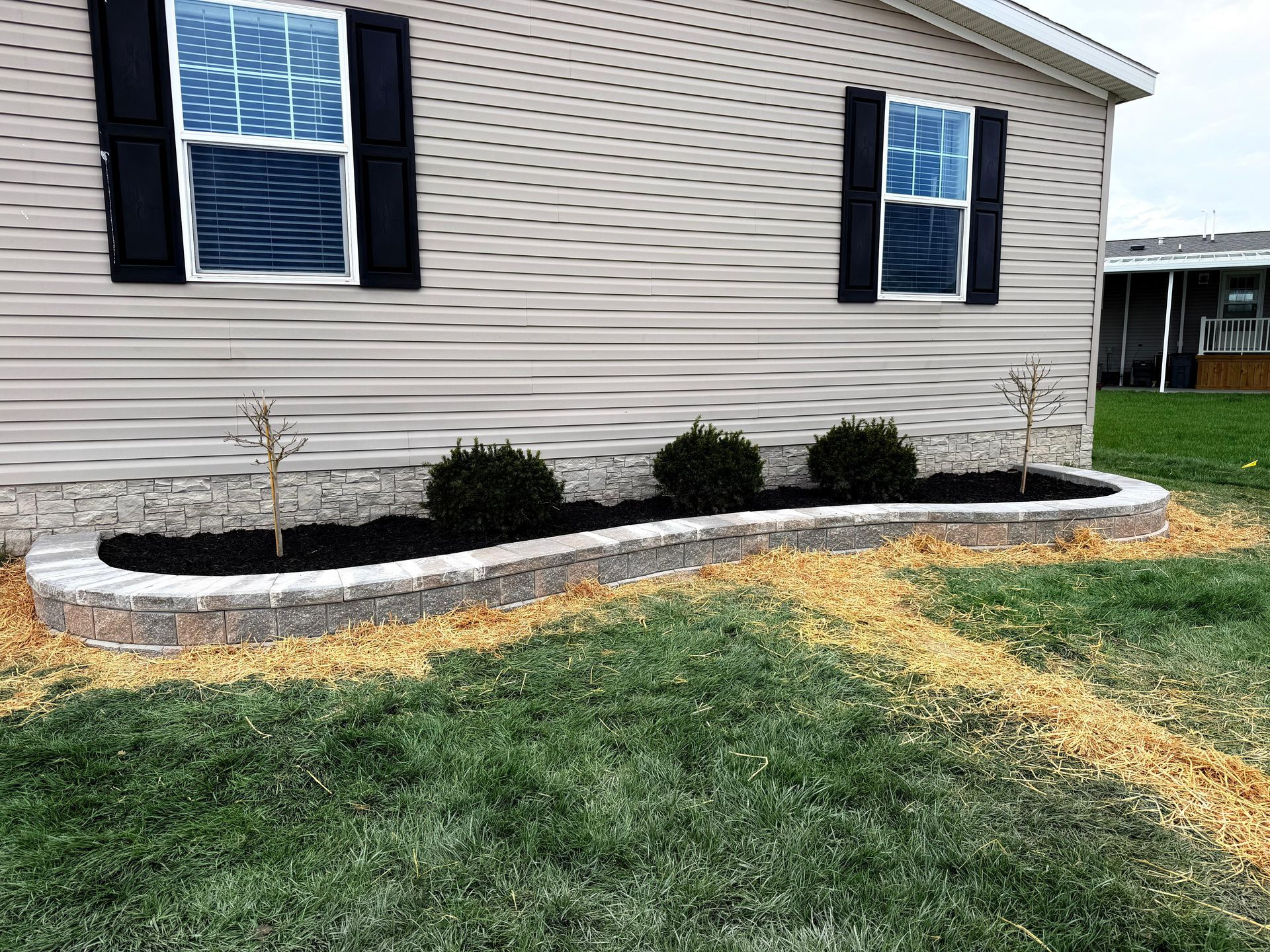 House exterior with black shutters, a window air conditioner, and a landscaped flower bed along the foundation