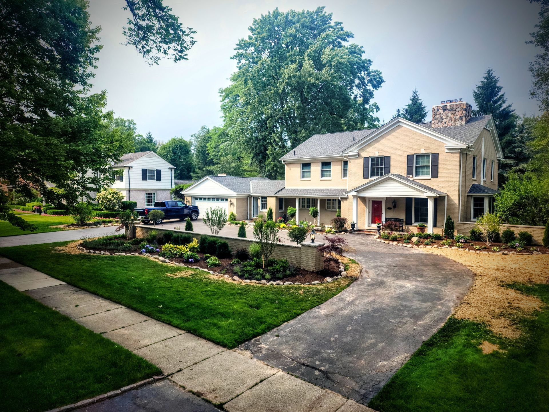 Suburban house with a curved driveway, landscaped yard, and trees under a clear sky