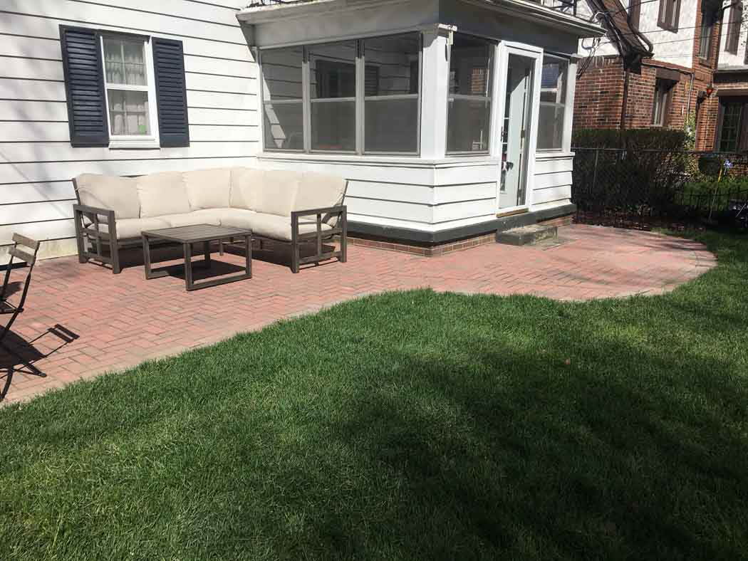 Backyard patio with white house, brick pavers, outdoor table and chairs beside a green lawn