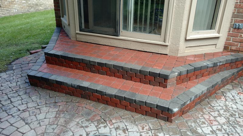 Brick steps leading to a beige building entrance with large windows and patterned paving stones