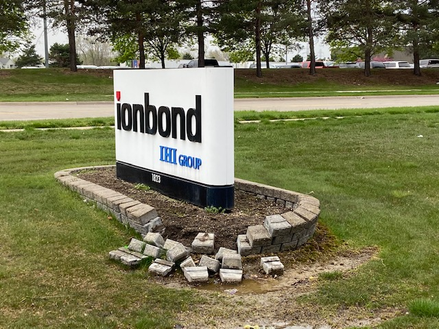 Ionbond company sign on a stone base beside a grassy roadside, with trees in the background.