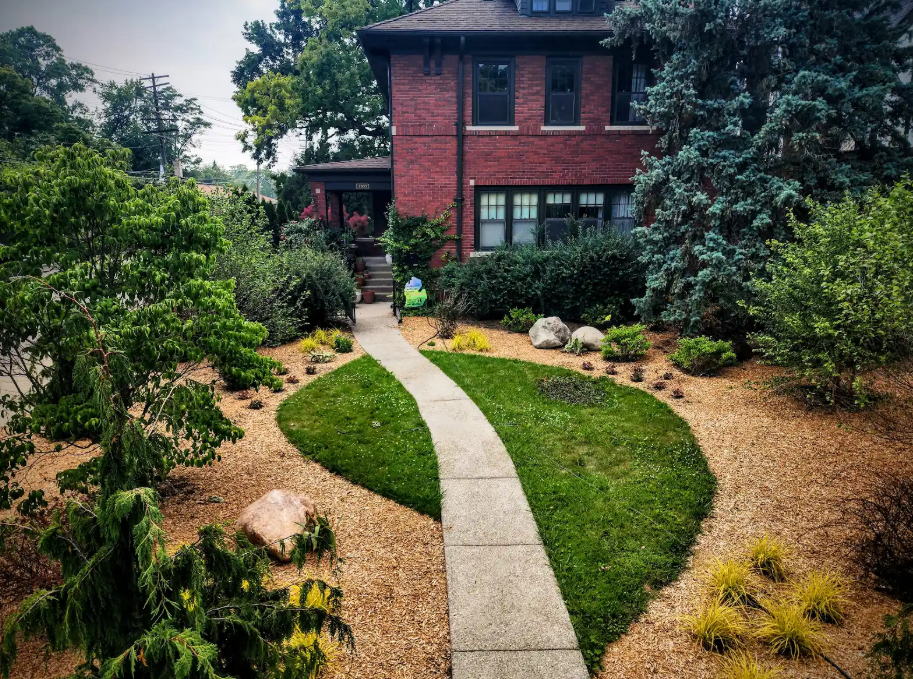 Brick house with a curved stone walkway through a lush green garden and trees