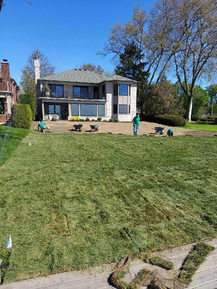 Two-story house with large sloped lawn and a person standing near the patio on a sunny day