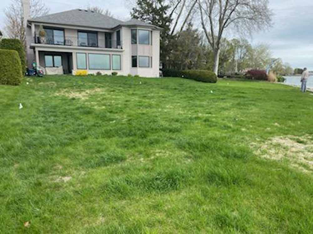 Two-story house with large grassy front yard and lakeside view on an overcast day