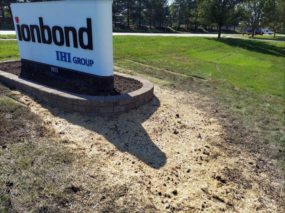 Ionbond sign beside a grassy roadside, with a brick base and bare dirt in front