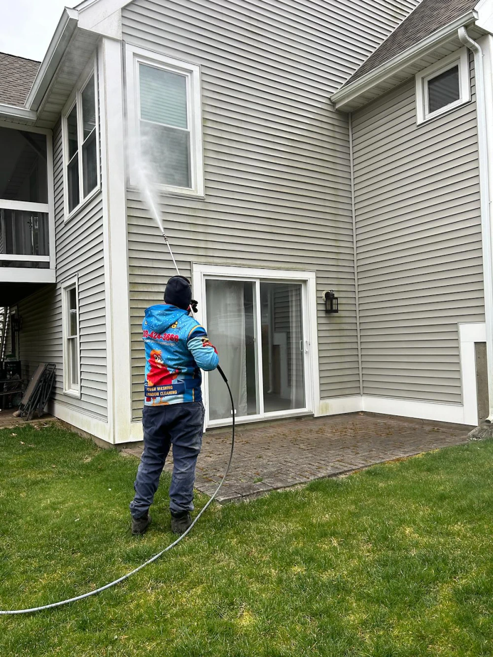 Person pressure-washes the side of a beige house from the lawn.
