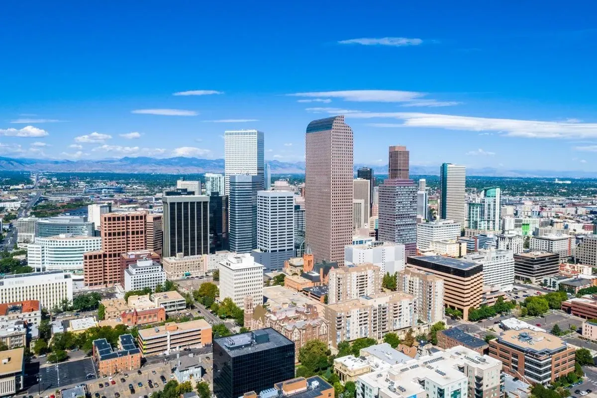 Denver, Colorado skyline with blue sky, modern buildings, and mountains in the distance.