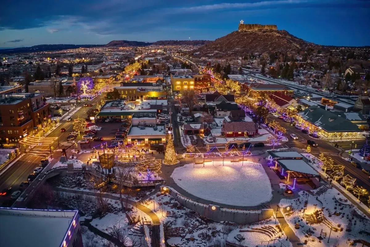Night aerial view of Bend, Oregon, with festive lights, snow, and Pilot Butte in the background.