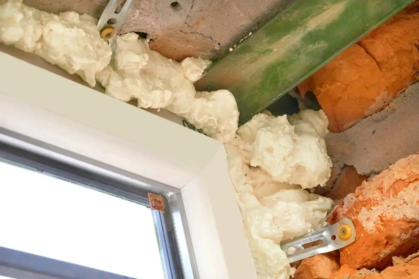 White foam insulation seals a window frame, covering brick and structural components.