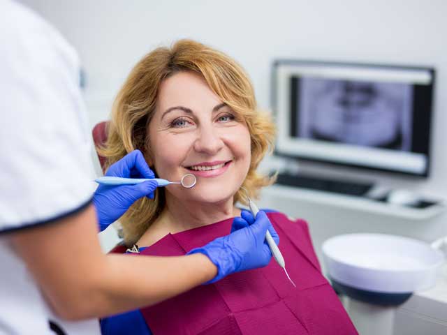 A woman is sitting in a dental chair while a dentist examines her teeth.