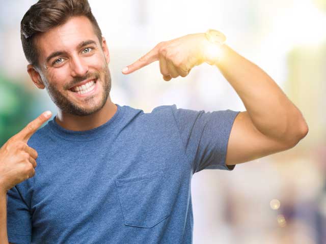 A young man is smiling and pointing at himself.