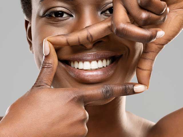 A woman is smiling and making a frame with her hands around her face.