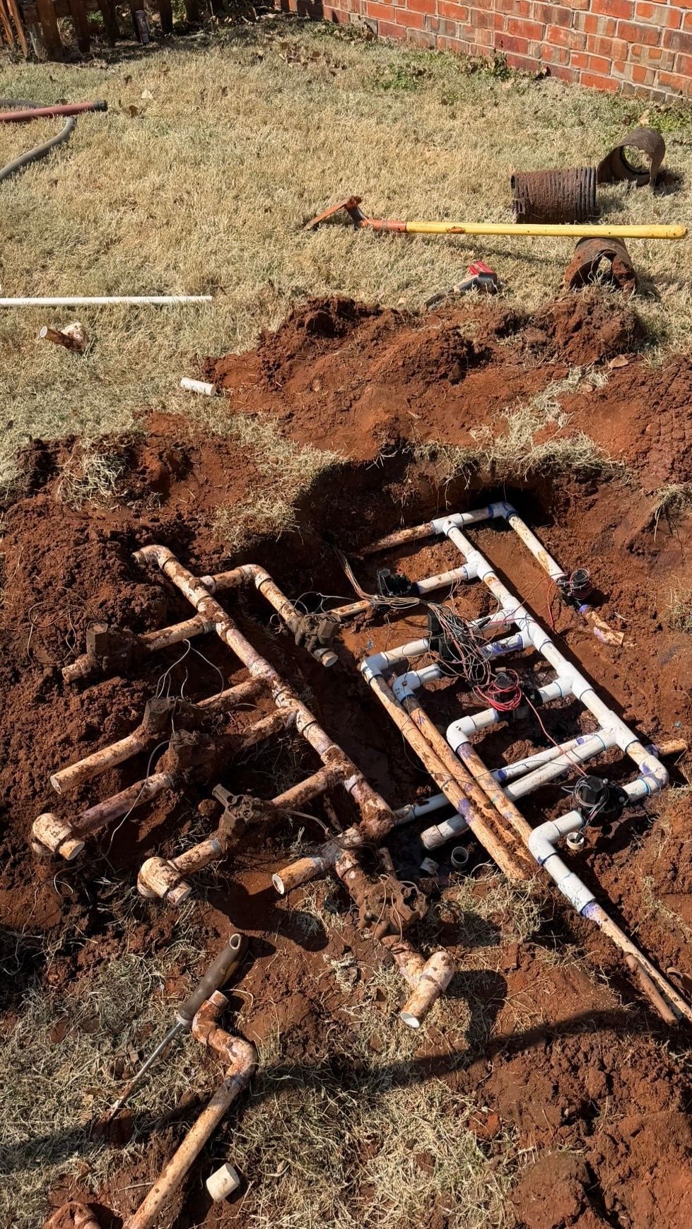 Exposed underground pipes and broken red soil in a dug-up yard near a brick wall