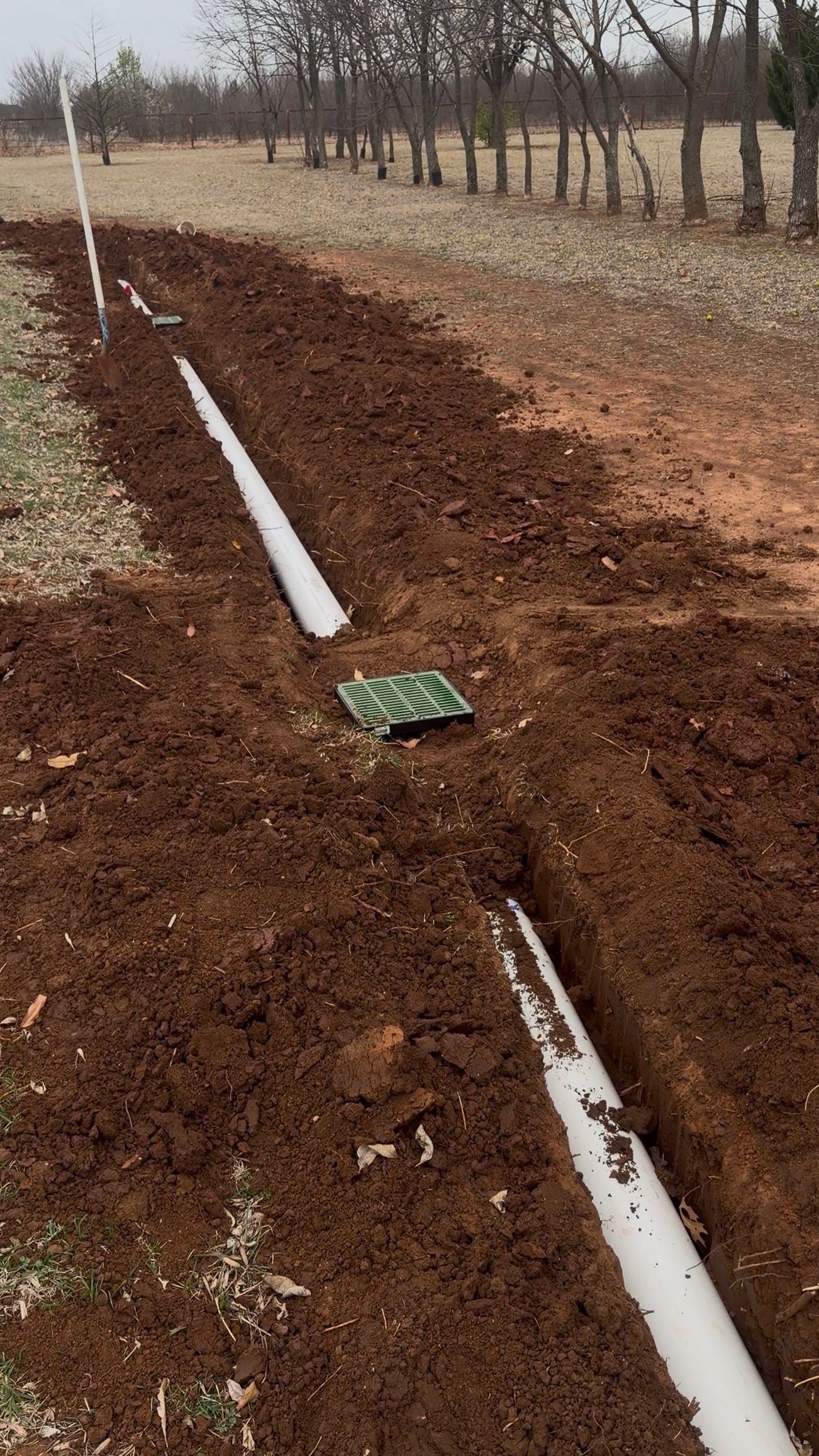 Freshly dug irrigation trench with white PVC pipe running through a muddy field