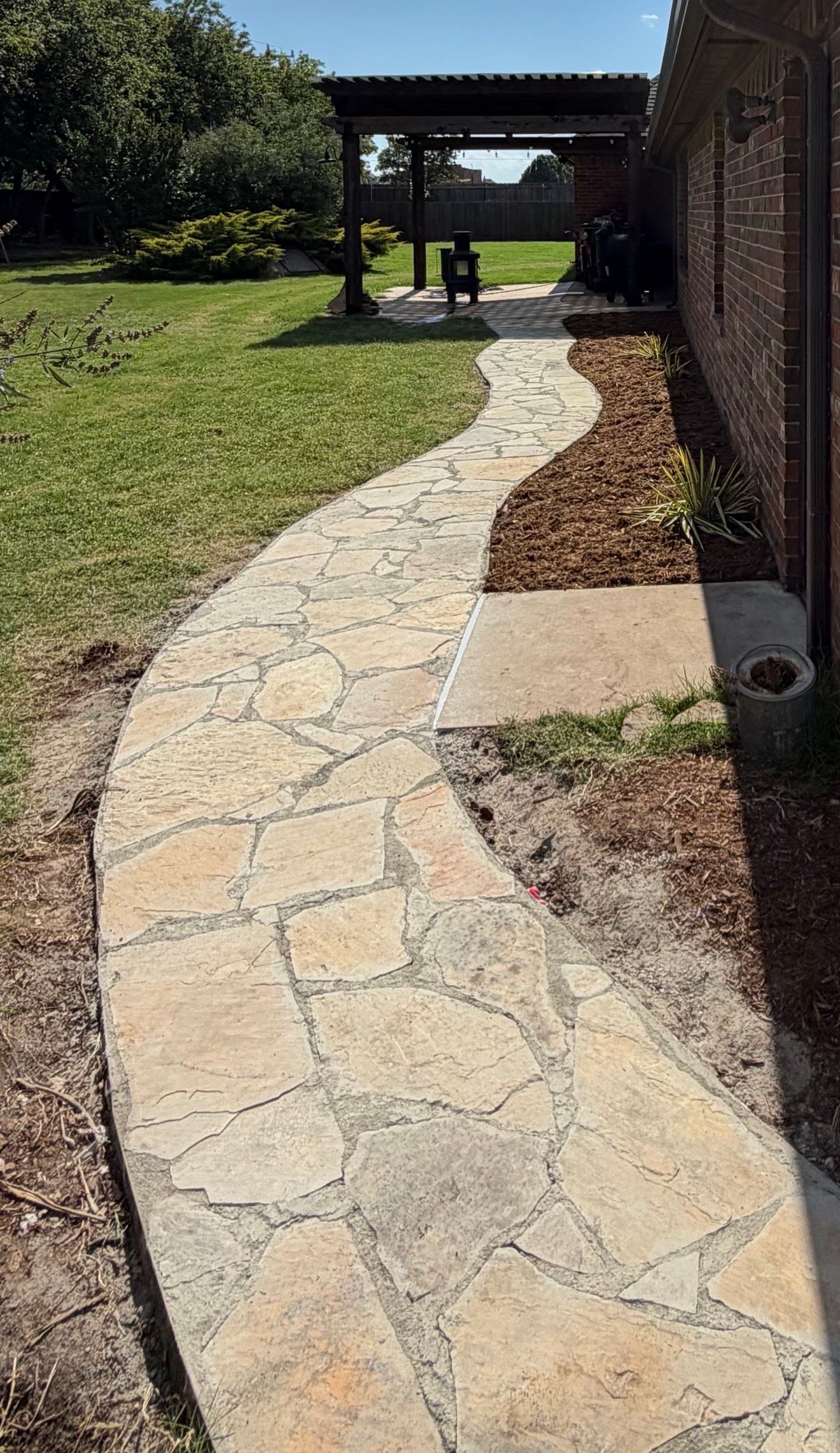 Curved stone pathway through a grassy yard leading to a covered patio