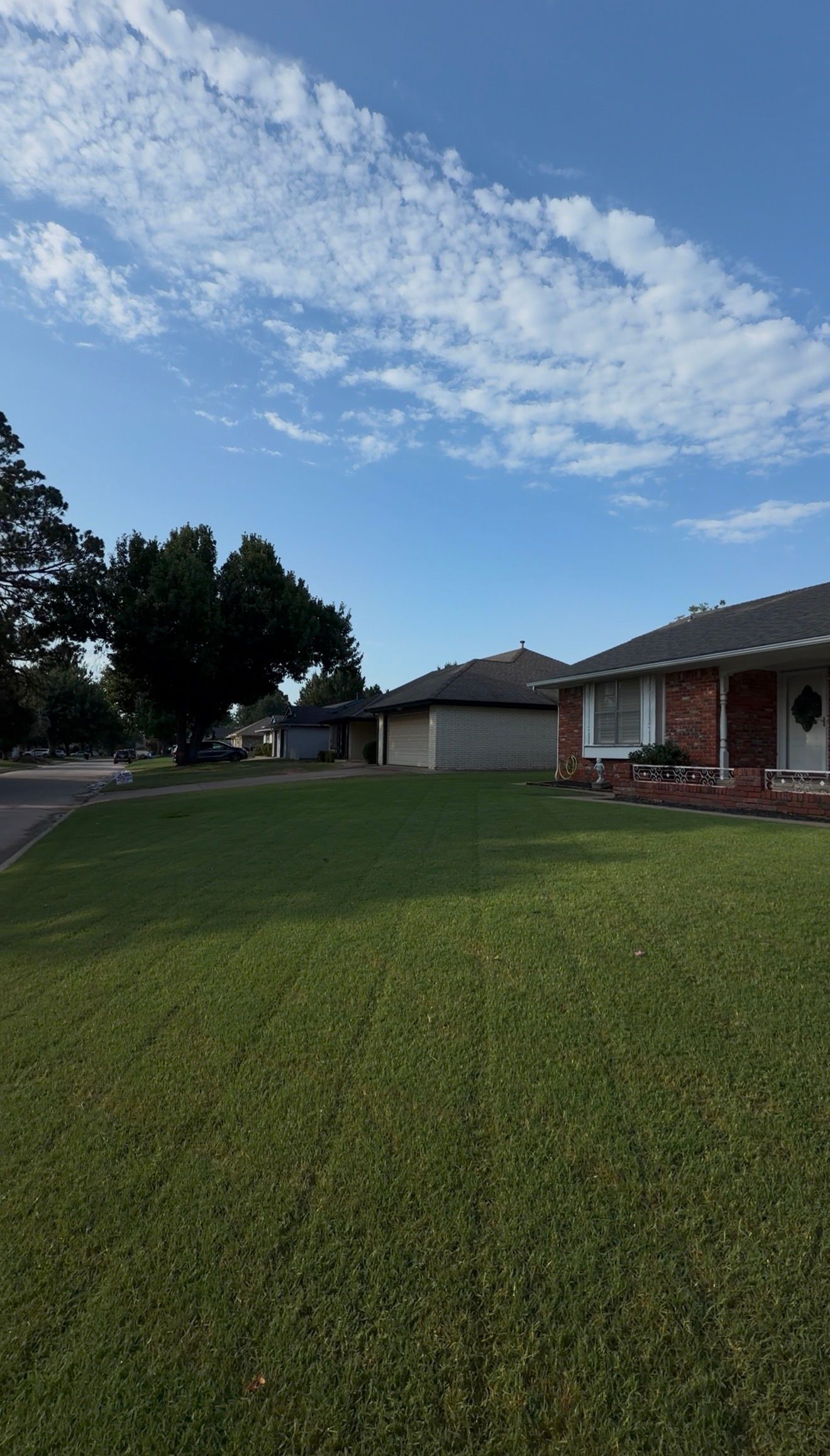 Suburban house with a large green lawn under a partly cloudy blue sky