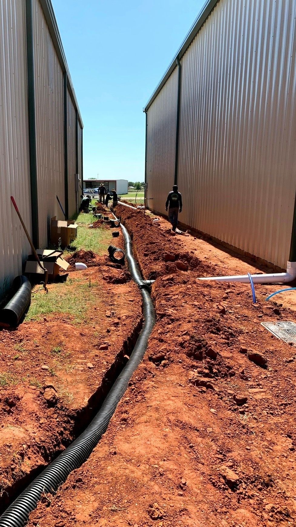 Narrow dirt path between tall metal walls with hoses on the ground and a person in the distance