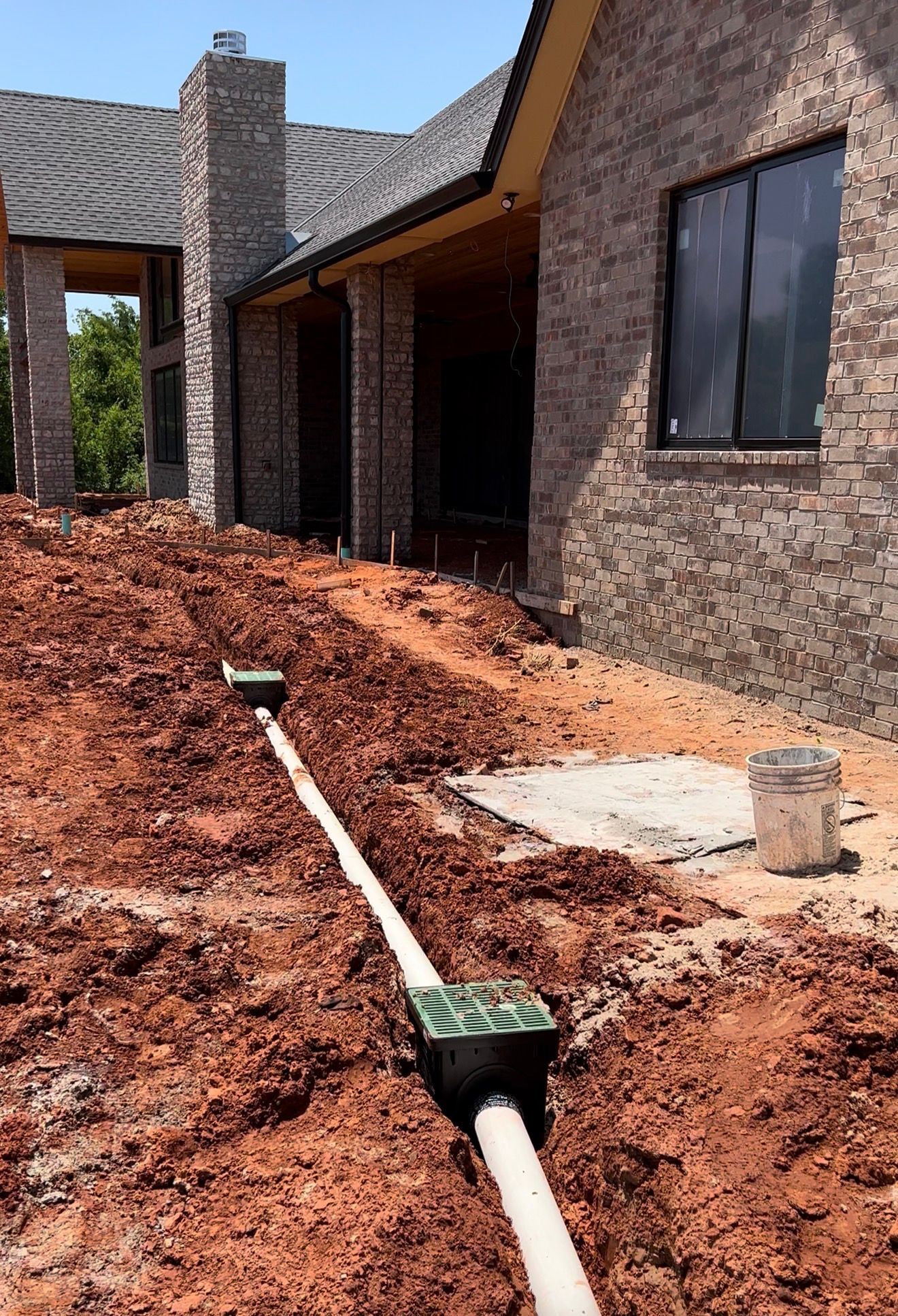 Unfinished brick house exterior with exposed dirt yard and a white drainage pipe in the foreground