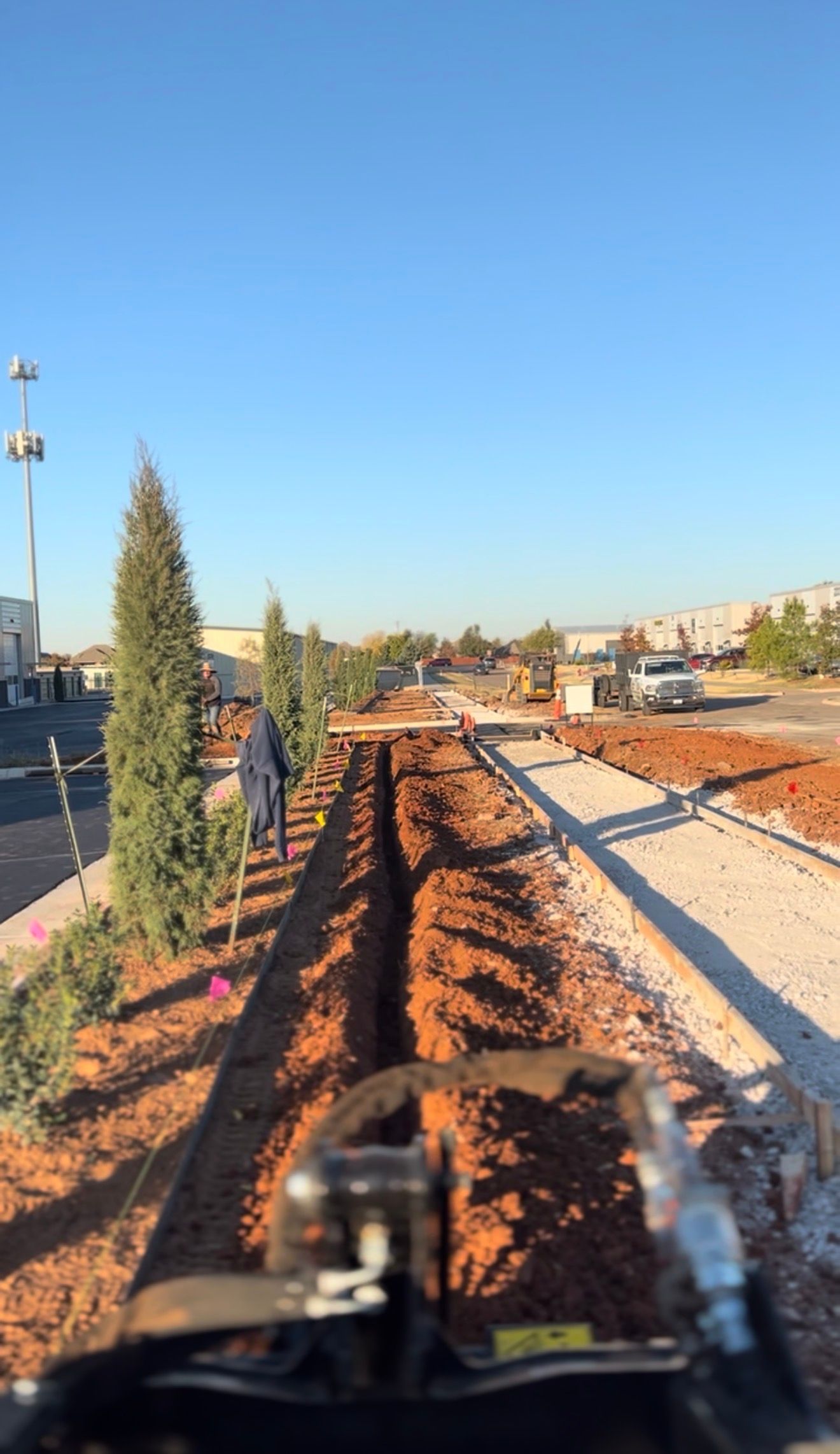 Railway construction site with red earth, gravel track bed, and a worker in a blue jacket under clear blue sky