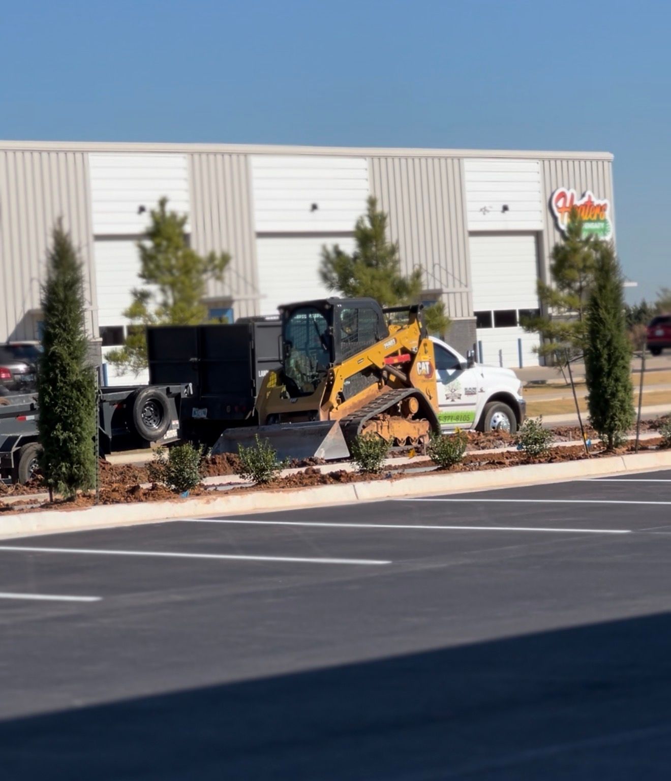 Skid steer and dump truck in a parking lot beside a white industrial building