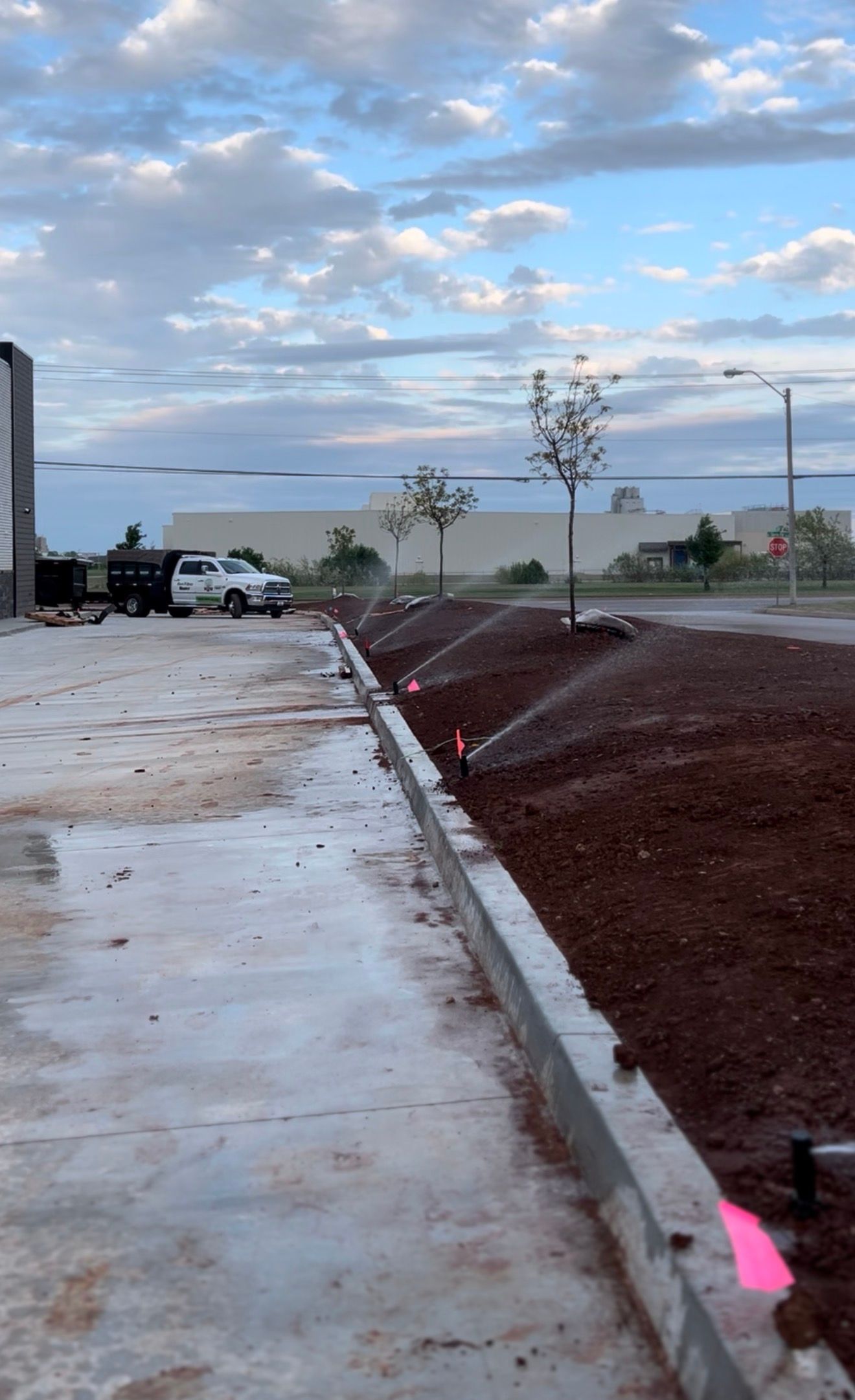 New concrete sidewalk beside a red dirt slope under a cloudy sky