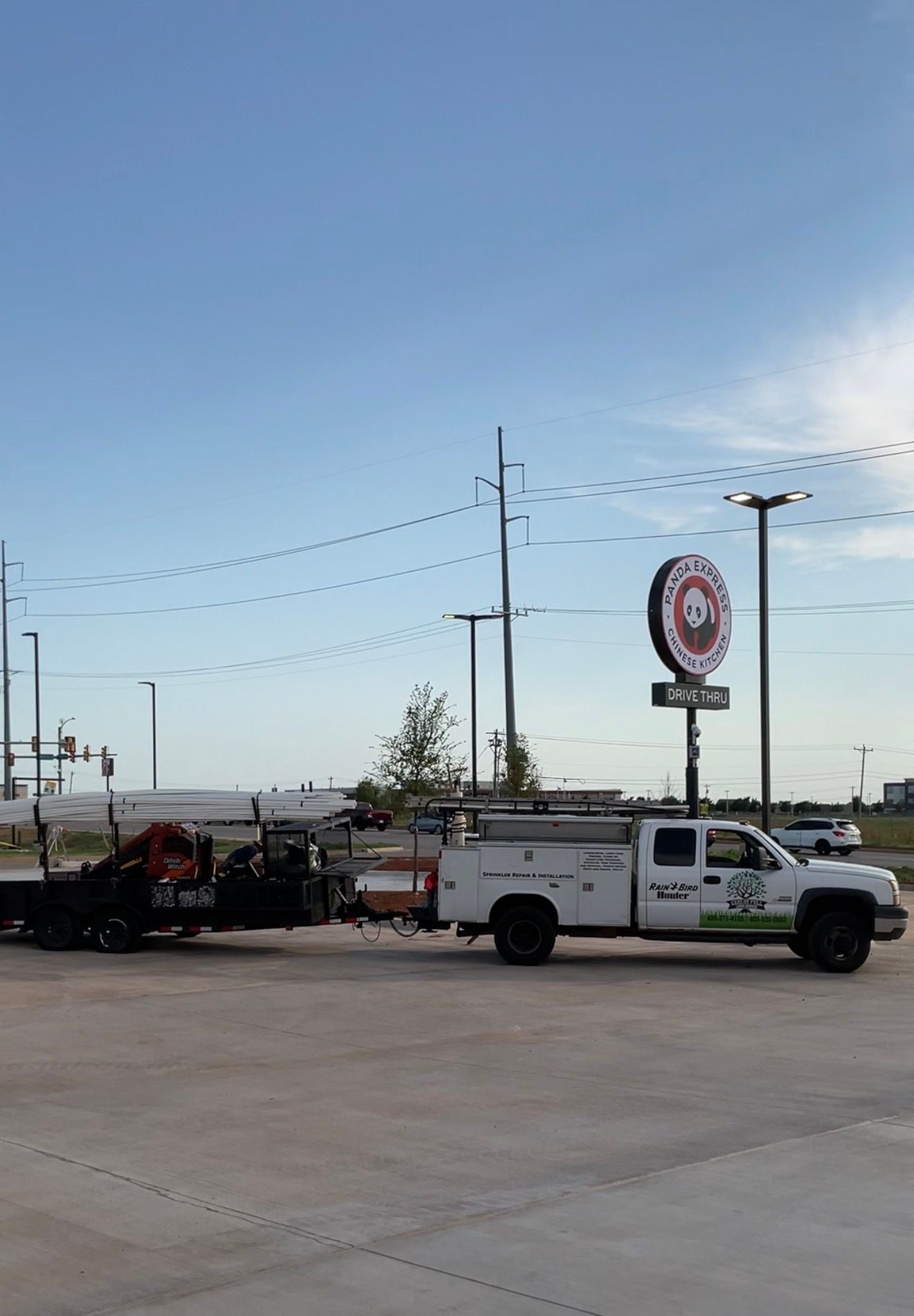 White utility truck towing equipment at a roadside store lot under a clear blue sky.